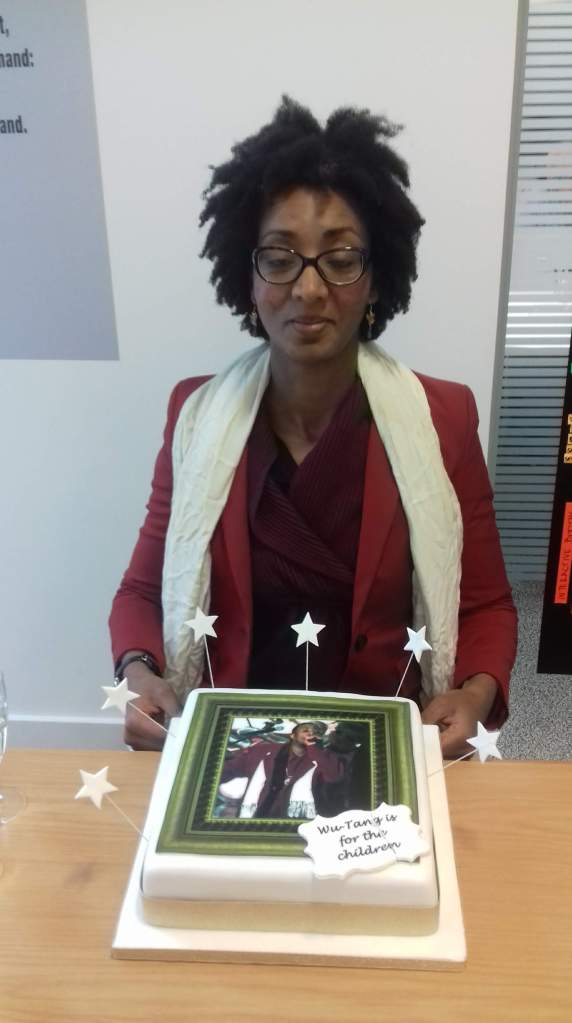 [decorative image] Photo of MG Zimeta facing the camera and seated at a table with a cake in front of her. Her eyes are closed. The cake has a large picture on it of the rapper ODB from the Wu Tang Clan.   The picture is from the 1998 Grammys when ODB rushed the stage to express regret that Wu Tang had not won the Best Album award, because he had bought this nice suit to celebrate the win, and where he coined the phrase "Wu Tang is for the children" (which is also on the side of the cake as a label made of icing).  MG Zimeta is wearing the same outfit as ODB.